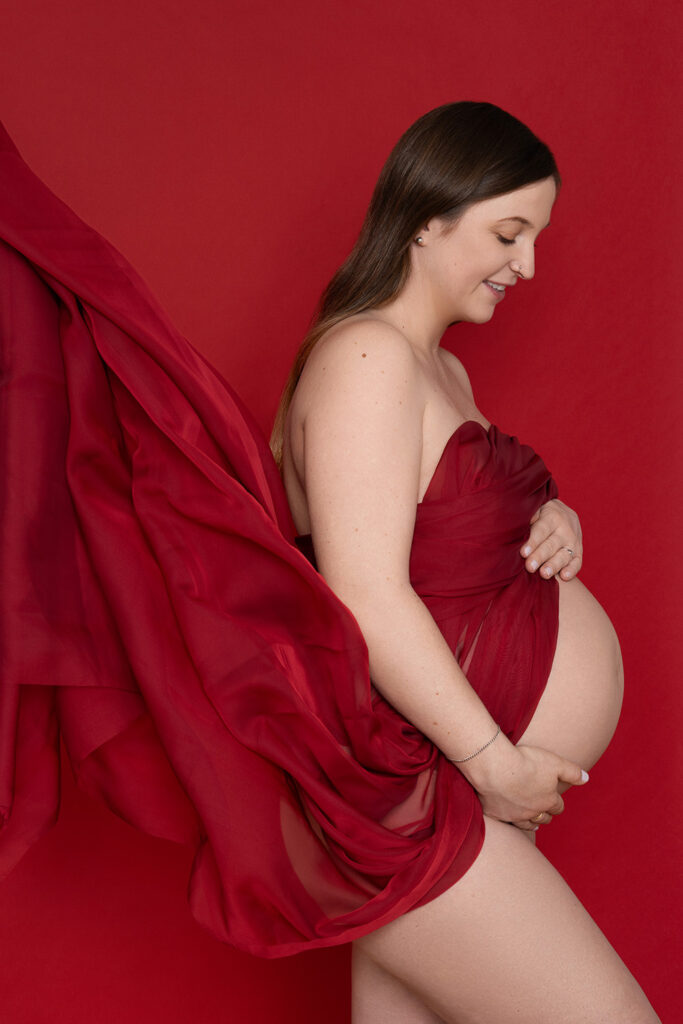 Eine Frau mit rotem Kleid bei einem Babybauch Fotoshooting im Fotostudio.
