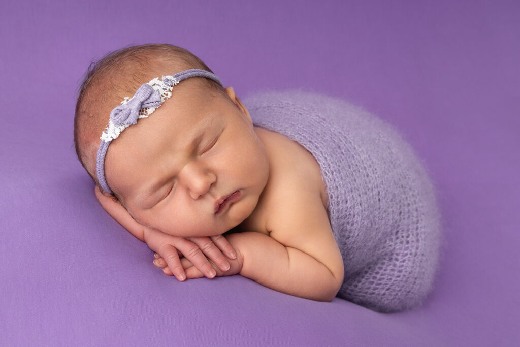 Ein Neugeborenes bei einem Fotoshooting schläft auf einer lila Decke.