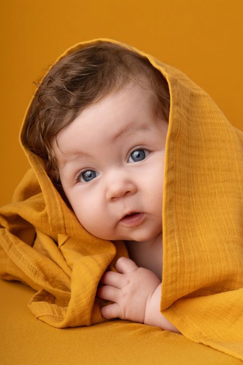 Ein vier Monate altes Baby unter einer gelben Decke bei einem Fotoshooting im Fotostudio.