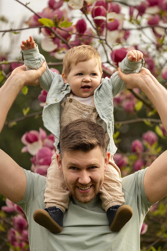 Ein einjähriger Bub auf den Schultern von seinem Papa bei einem Fotoshooting.