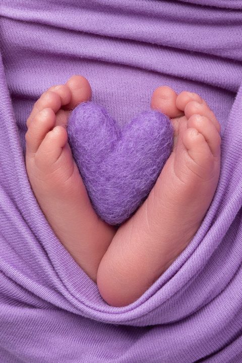 Babyfüße halten ein lila Herz.