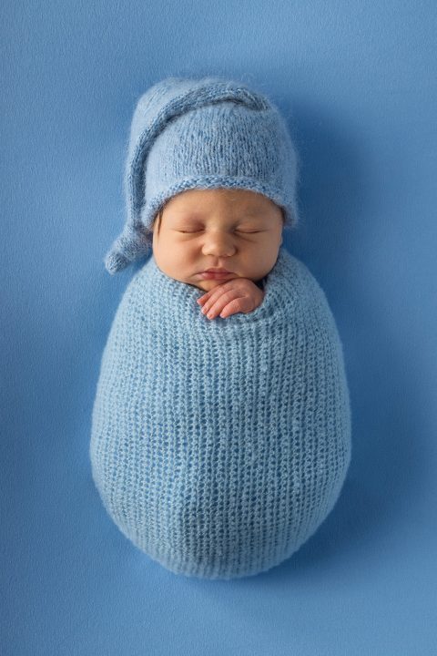 Ein neugeborenes Baby liegt eingewickelt in einer gehäkelten Decke bei einem Newborn Fotoshooting.