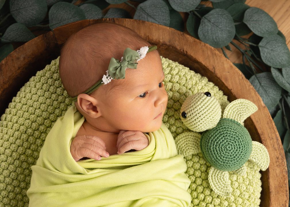 Ein Baby schaut eine gehäkelte Schildkröte an bei einem Newborn Fotoshooting.