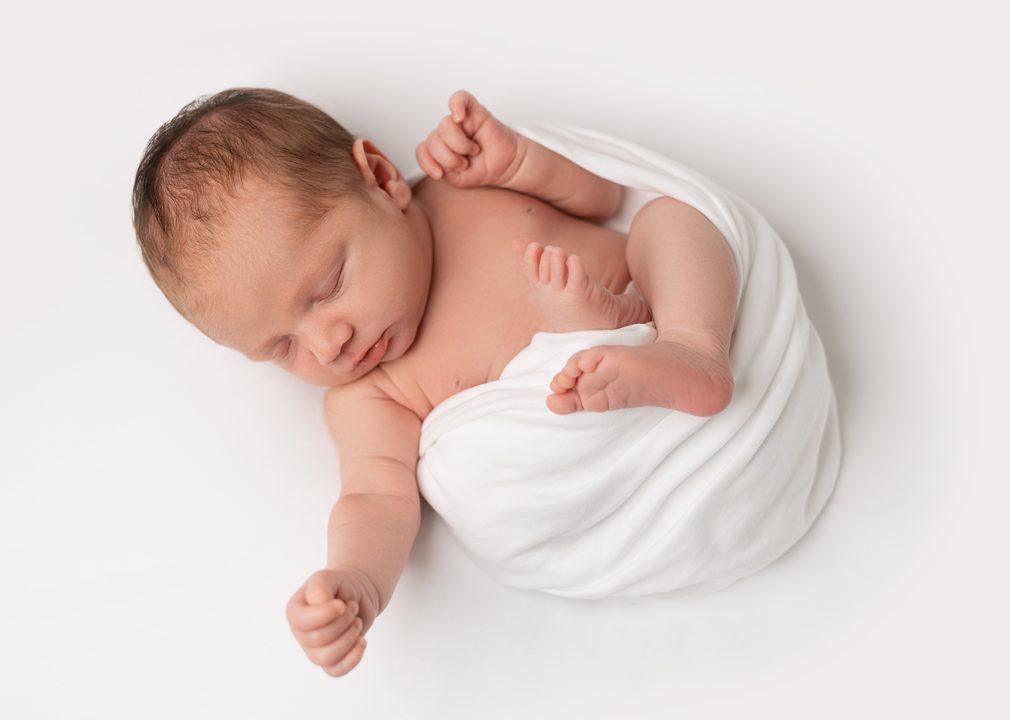 Ein neugeborenes Baby in weiß bei einem Newborn Shooting im Fotostudio.